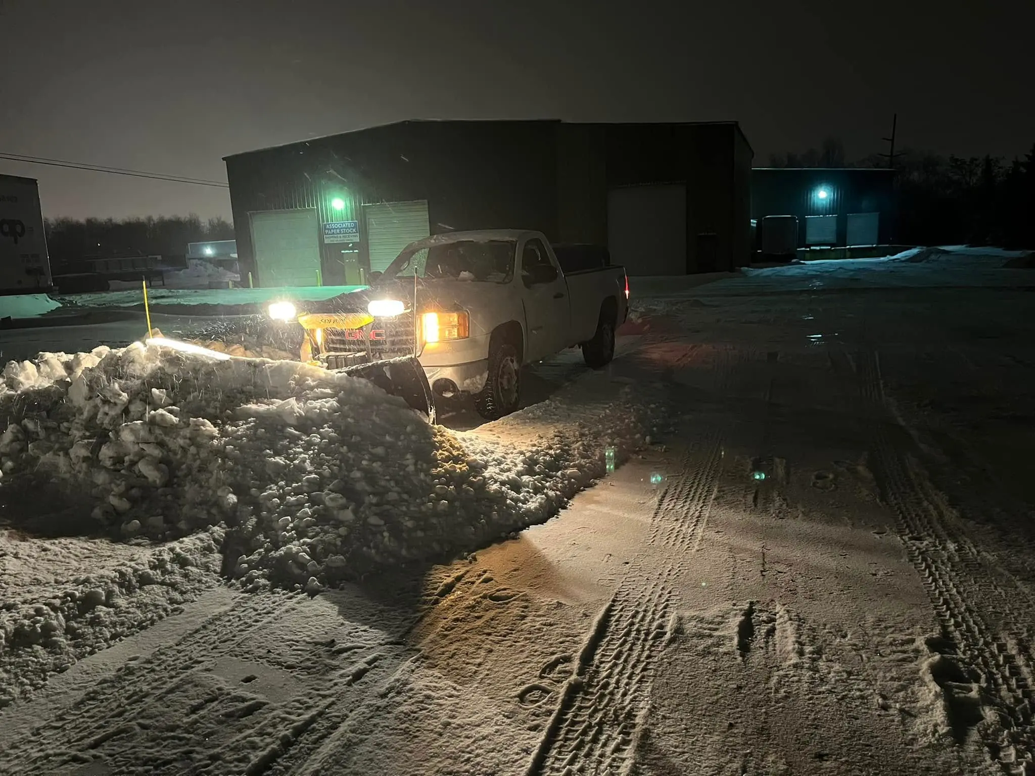 Truck plowing snow at night in commercial parking lot during winter storm