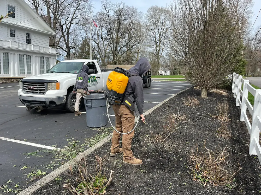 Technician performing weed control and spraying landscape beds along a parking area