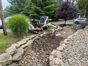 Mini excavator performing yard grading and drainage work with stone and soil preparation